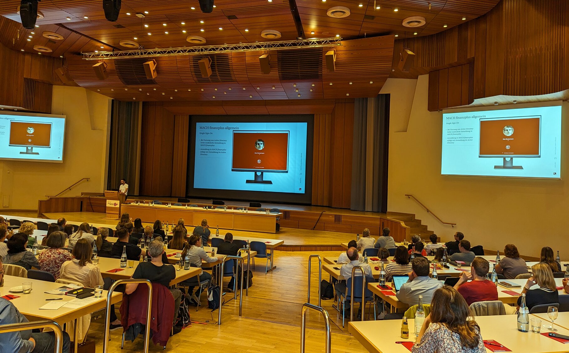 Ein großes Auditorium mit Menschen, die an Tischen sitzen und an einer Veranstaltung teilnehmen